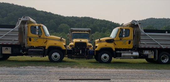 Three WV DOT dump trucks parked beside a road