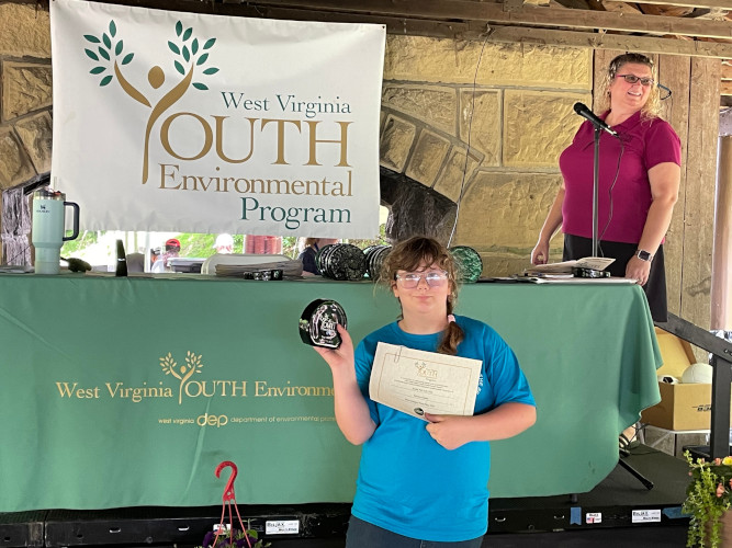 A representative from the Sandy Pals 4-H Club in Preston County holds up a certificate and glass award.