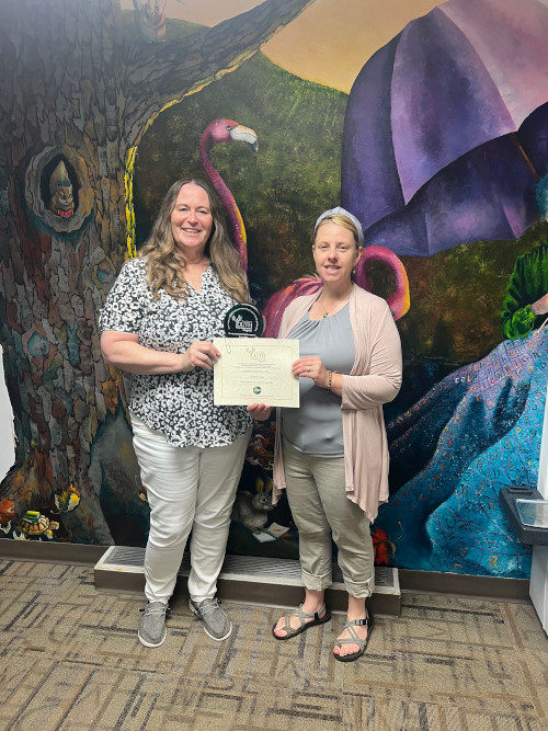 An employee of the Hampshire County Public Library holds up a certificate, while standing next to Susan Carroll of the DEP's Youth Environmental Program.