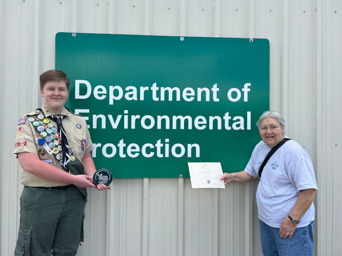 A member of Troop 32 from Hampshire County holds up a glass award, while the troop leader displays a certificate.