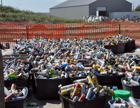 Tens of plastic totes full of of old and rusting metal aerosol cans near a landfill.